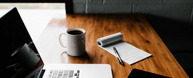 MacBook Pro, white ceramic mug,and black smartphone on table